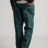 A person shown from the waist down wearing dark teal blue denim jeans, a black knit sweater, a striped shirt, and black shoes, standing against a white wall.