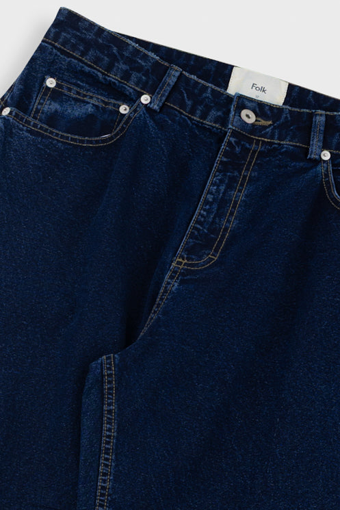 Close-up of dark blue jeans with a visible brand label on a white background