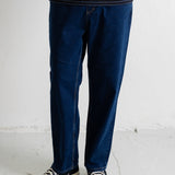 A person wearing dark blue straight-leg jeans, a navy and white striped t-shirt, and navy canvas sneakers with white soles, standing against a white wall.