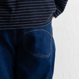 Close-up of a person wearing dark blue jeans with a back pocket and a navy striped top against a white wall.