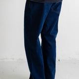 A person shown from the waist down wearing dark blue straight-leg jeans, a navy and white striped t-shirt, and black canvas sneakers with white soles, standing against a white wall.
