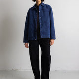 A model stands in a studio wearing a blue corduroy jacket over a black shirt and black trousers.