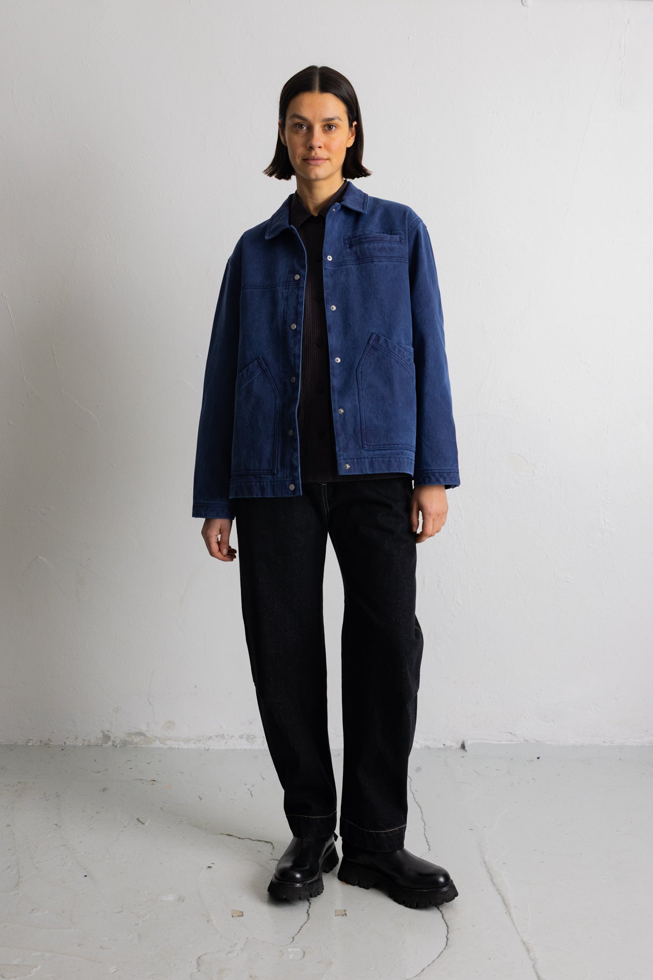 A model stands in a studio wearing a blue corduroy jacket over a black shirt and black trousers.