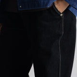 Close-up of a person wearing dark indigo denim jeans with contrast stitching and a blue denim jacket partially visible at the top.