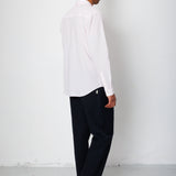 Man wearing a white shirt and black pants against a white wall