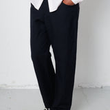 Person wearing a white shirt, black pants, and black sneakers against a plain background