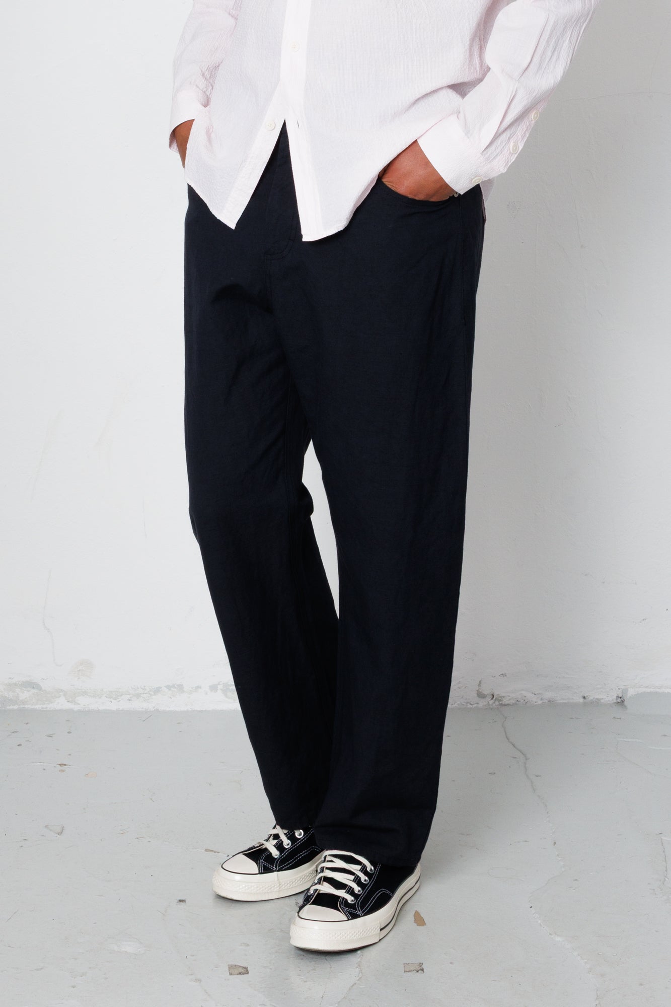 Person wearing a white shirt, black pants, and black sneakers against a plain background