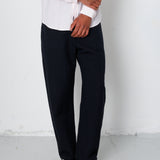 Person wearing a white shirt, black pants, and black sneakers against a plain background