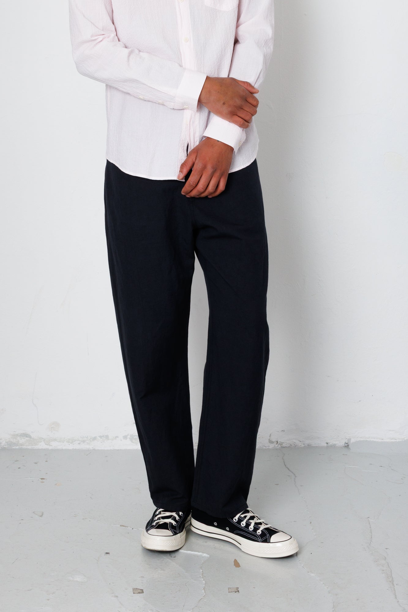 Person wearing a white shirt, black pants, and black sneakers against a plain background