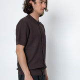 Man wearing a brown textured shirt and dark pants against a white background