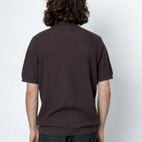 Person wearing a brown textured shirt and dark pants against a white background
