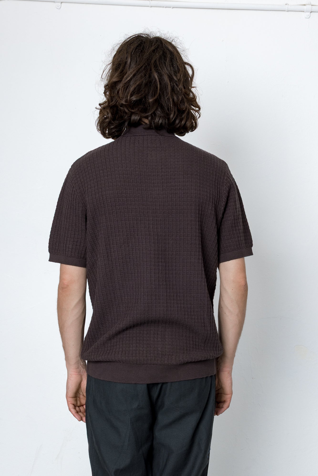Person wearing a brown textured shirt and dark pants against a white background
