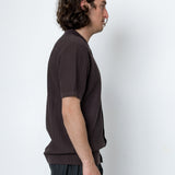 Man wearing a brown textured shirt and dark pants against a white background