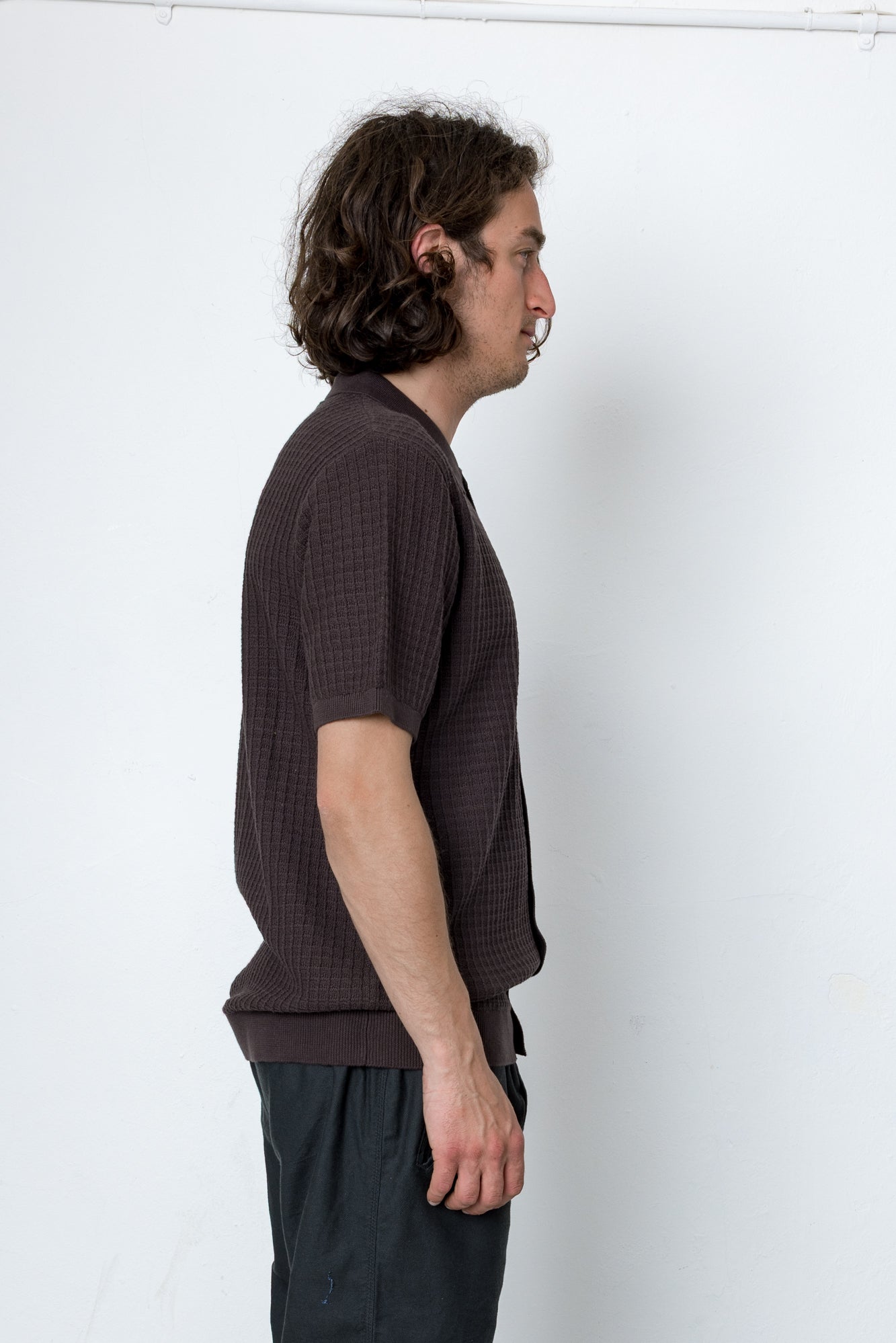 Man wearing a brown textured shirt and dark pants against a white background