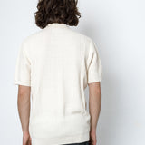 Person wearing a white ribbed sweater against a plain white background