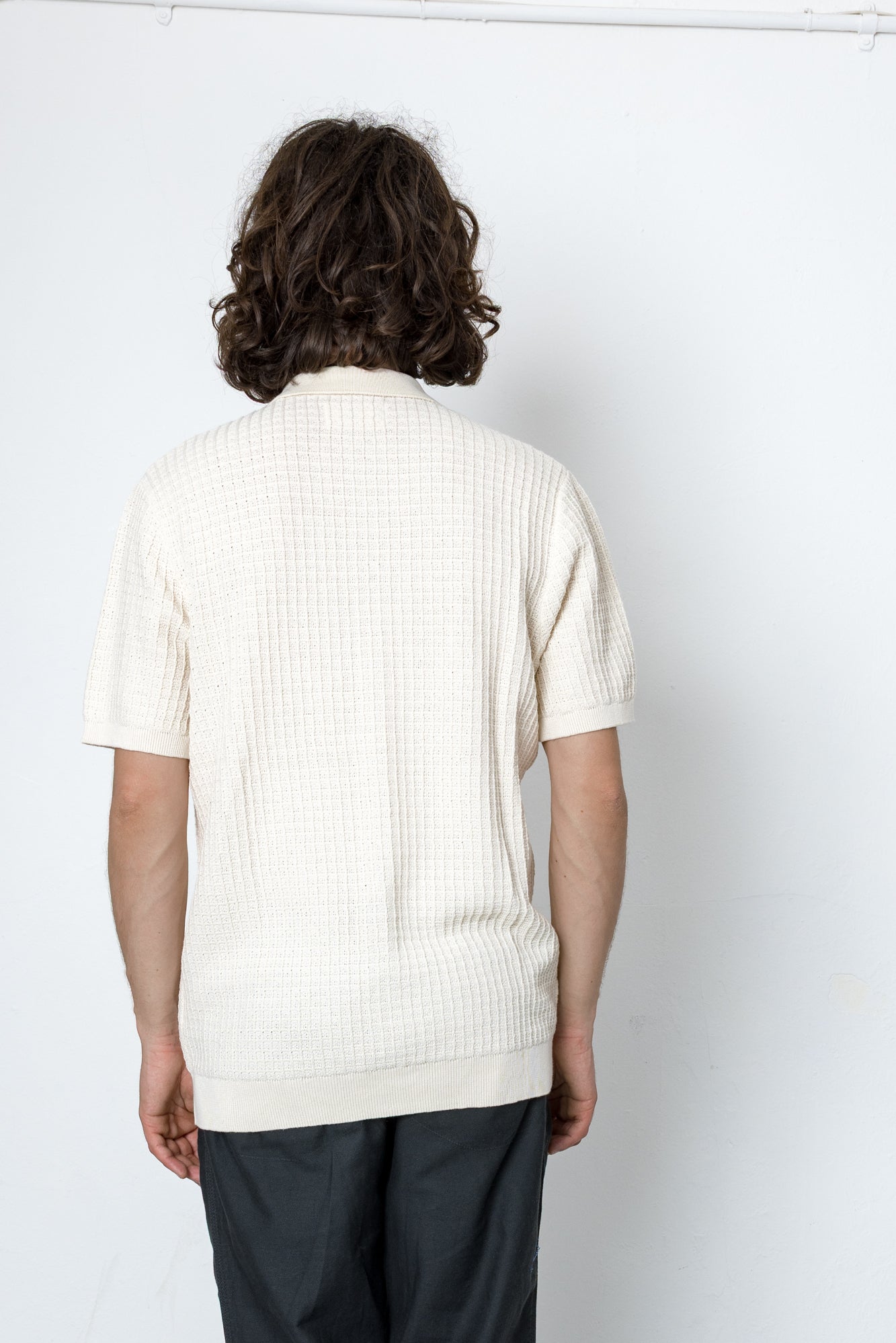 Person wearing a white ribbed sweater against a plain white background