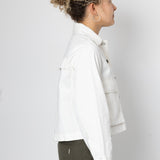 Woman wearing white jacket and green trousers against a grey background
