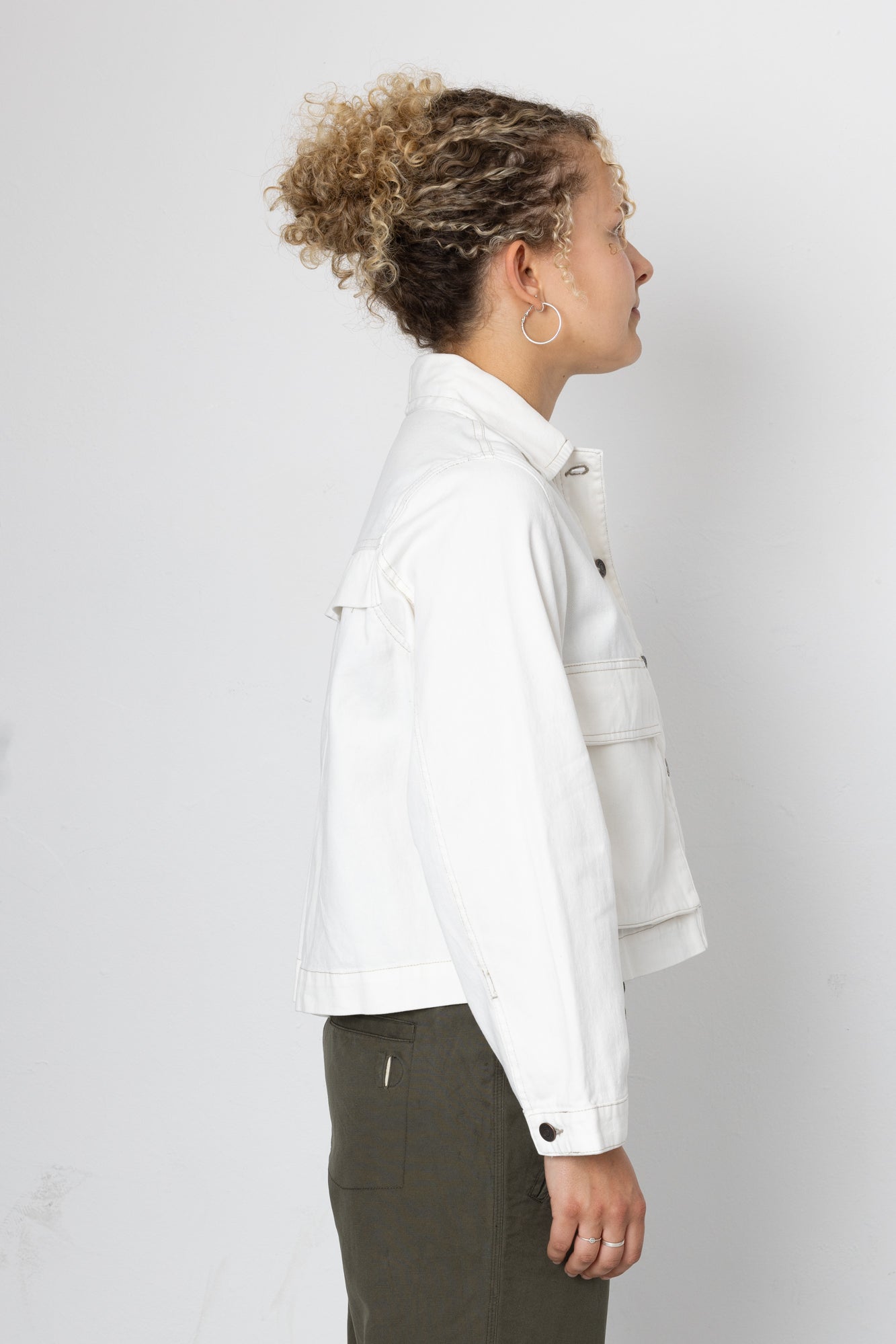 Woman wearing white jacket and green trousers against a grey background