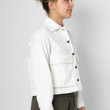 Person wearing a white jacket with black buttons on a plain background