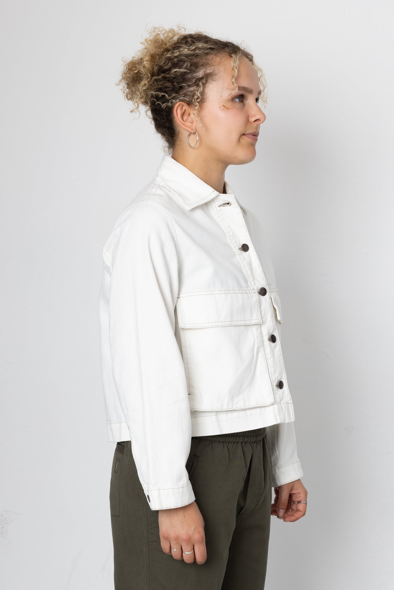 Person wearing a white jacket with black buttons on a plain background