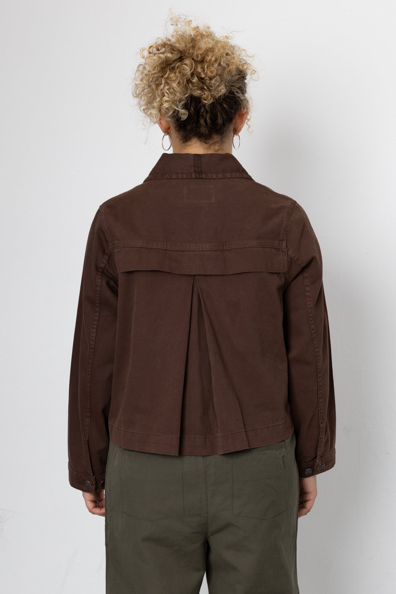 Person wearing a brown jacket and green pants against a white background
