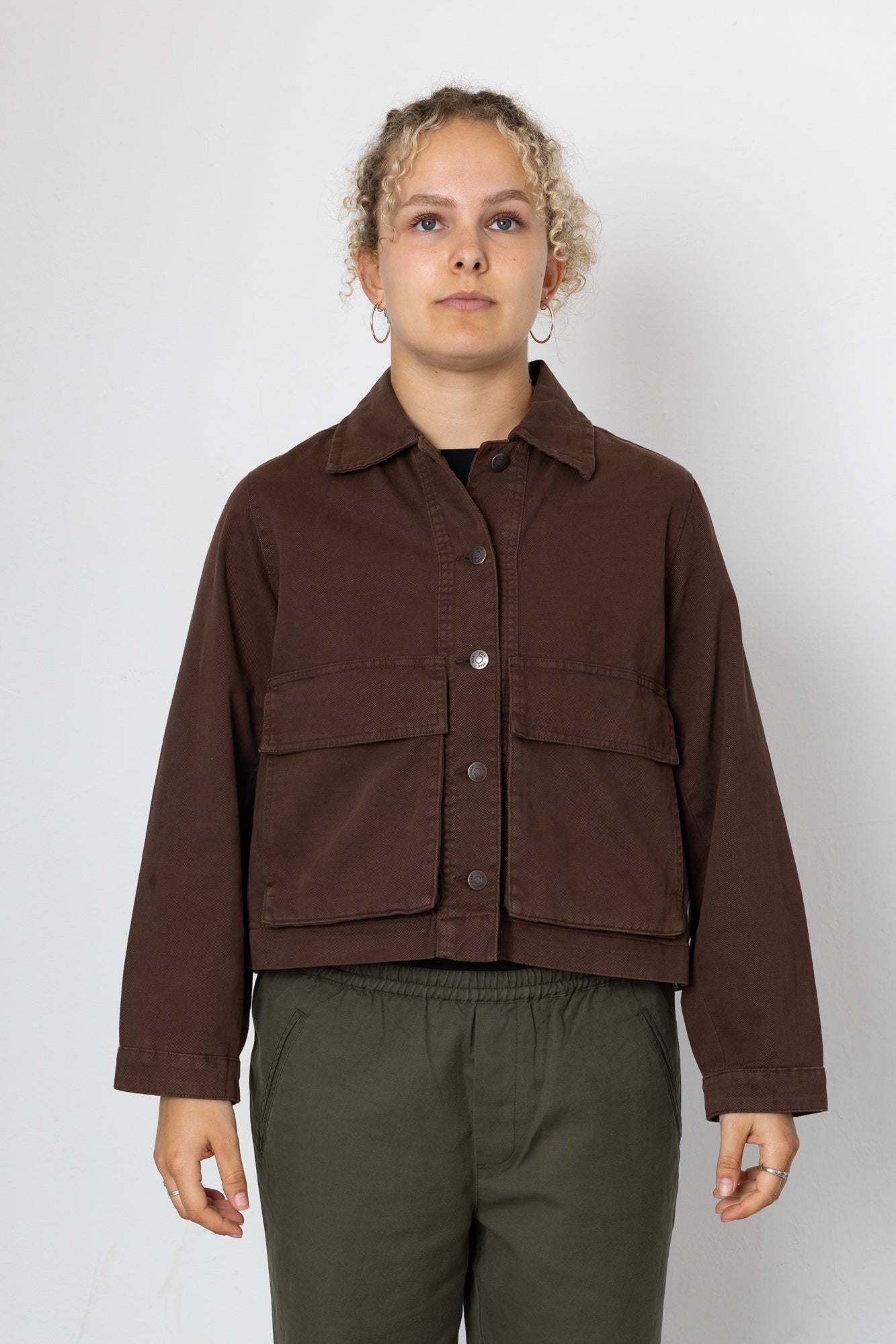 Person wearing a brown jacket and green pants on a white background