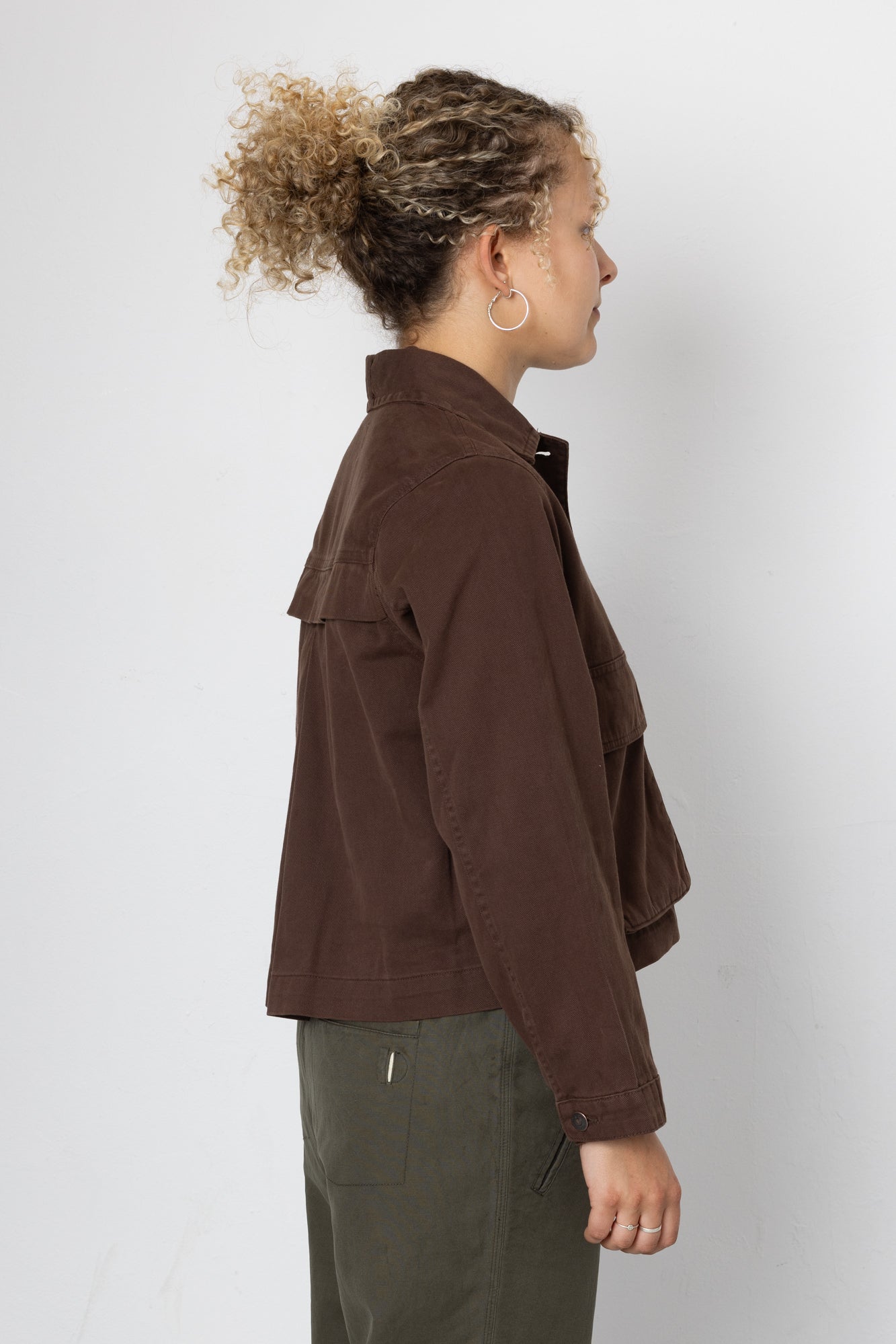 Person wearing a brown jacket and green pants on a white background