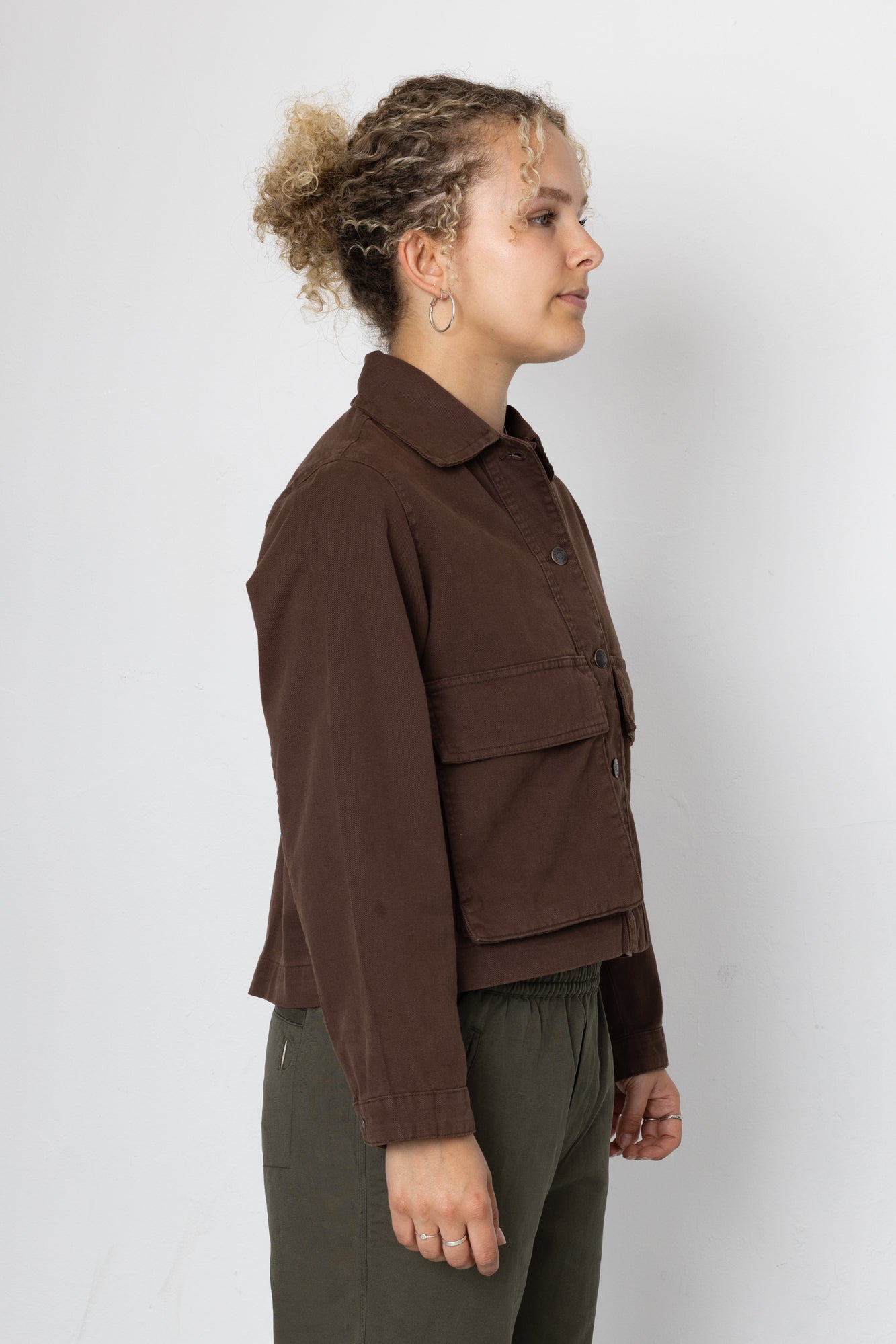 Person wearing a brown jacket and green pants against a white background