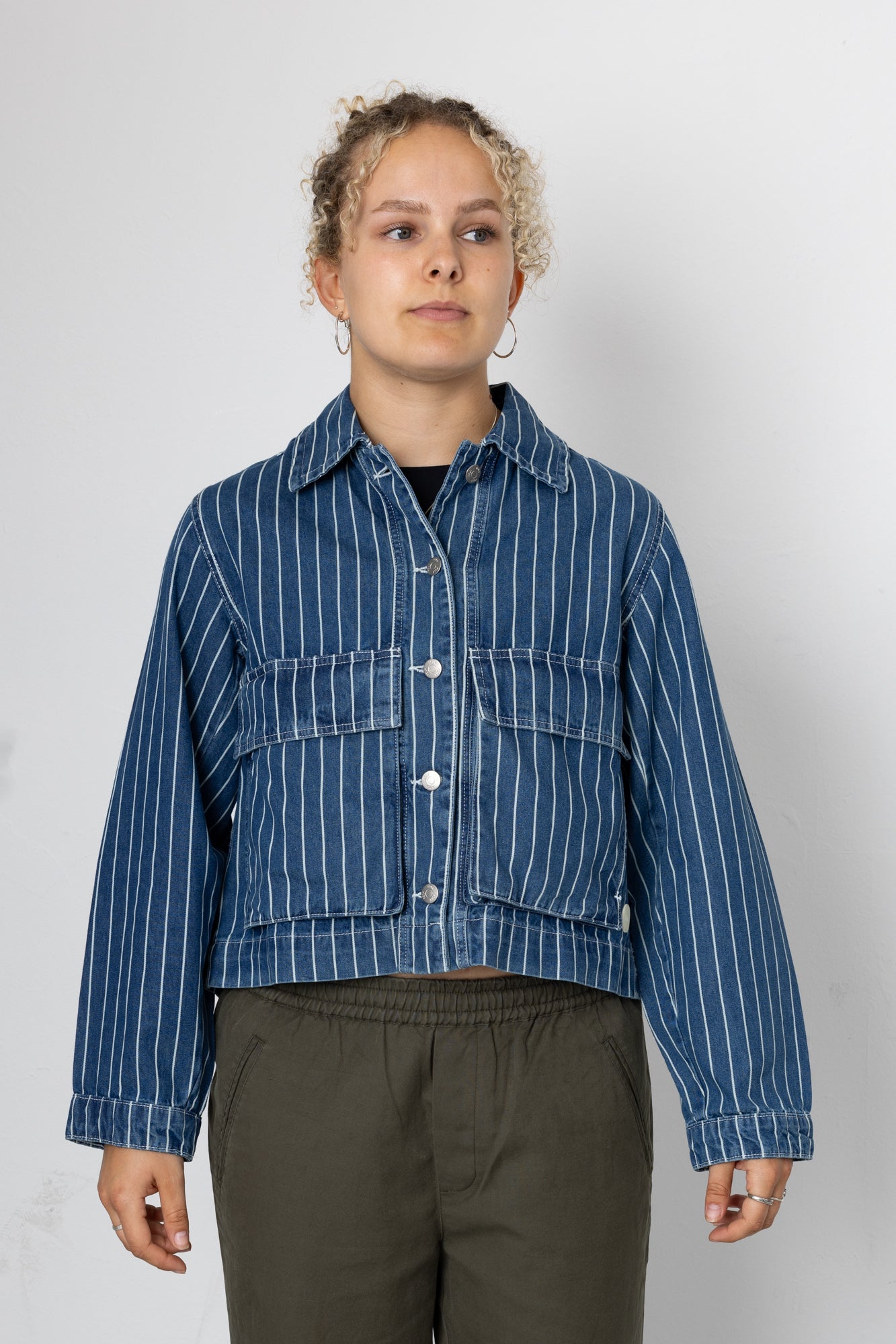 Person wearing a blue striped denim jacket against a white background