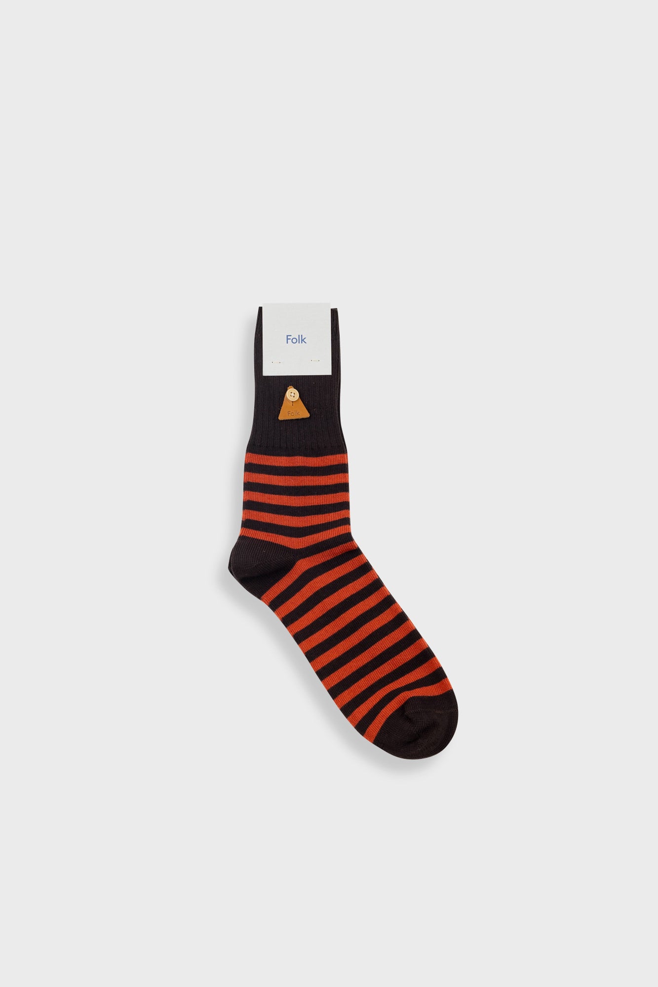A single sock with horizontal orange and black stripes, a black toe and heel, and a small gold geometric logo near the cuff, shown on a light gray background with a white paper label attached.