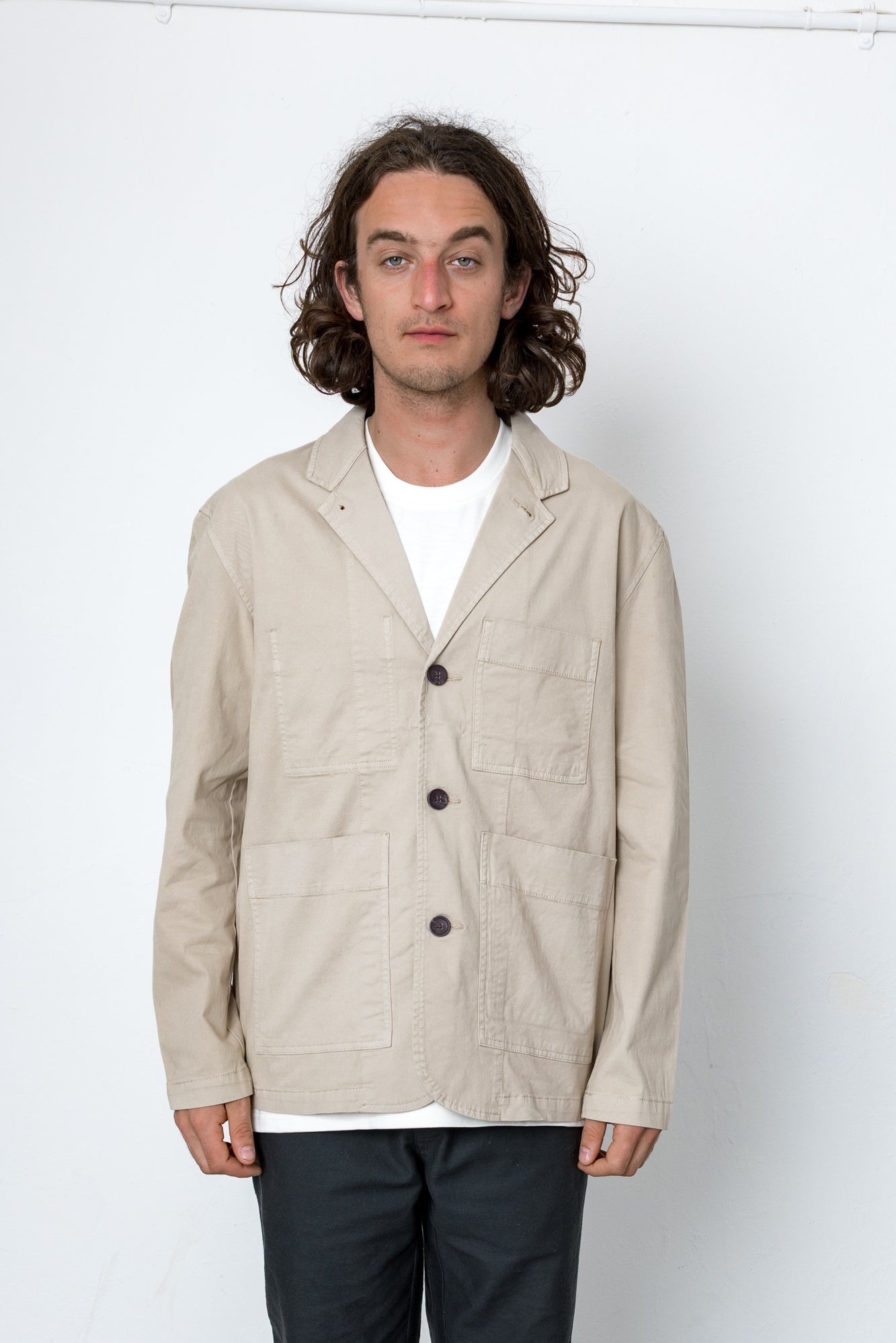 Man wearing a beige jacket over a white shirt on a white background