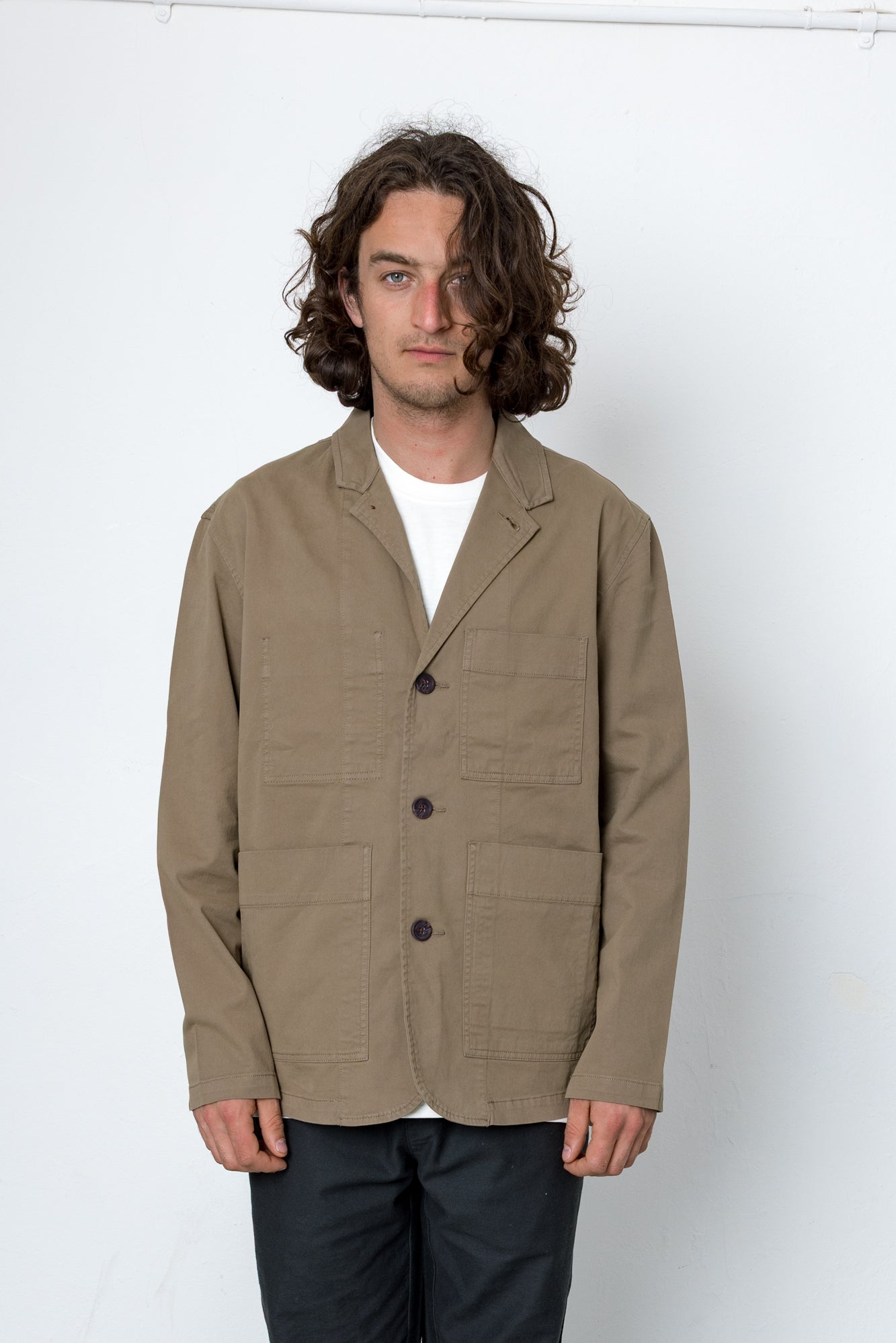 Man wearing a beige jacket over a white shirt on a white background