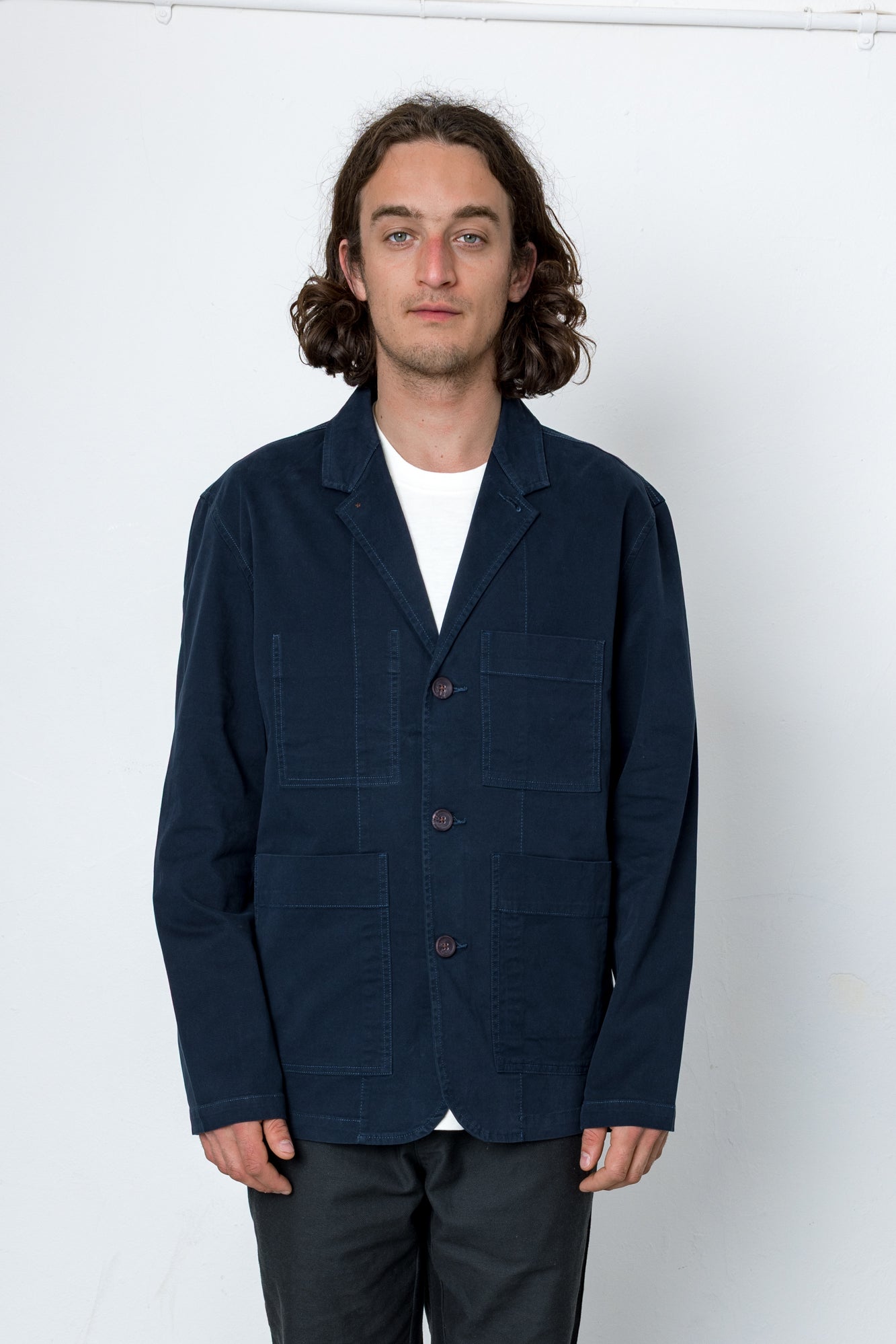 Man wearing a navy blue jacket over a white shirt on a white background