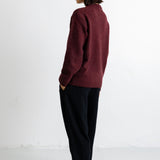 A model is shown from the back wearing a maroon knit sweater and black trousers, standing against a plain white studio background.