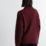 A person shown from the back wearing a dark burgundy knit sweater and black pants against a plain white wall.