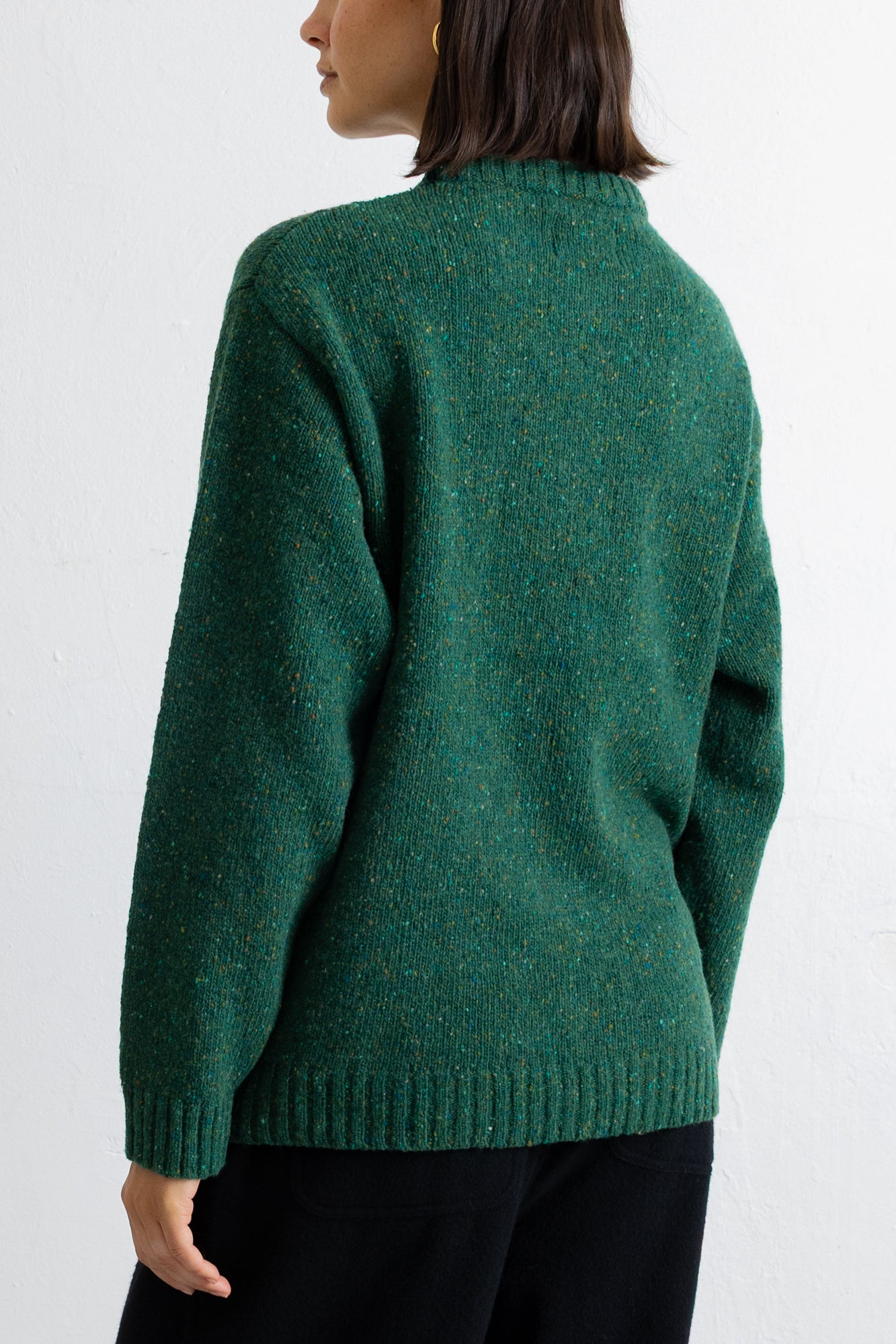 A woman wearing a textured green knit sweater, shown from the back against a plain white background.