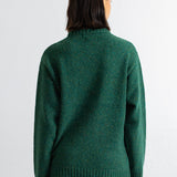 A person shown from the back wearing a dark green knit sweater and dark pants against a plain white studio background.