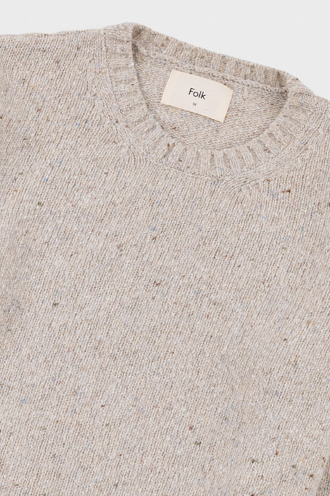 Close up of a cream coloured knitted jumper, showing the ribbed detailing on the crew neckline