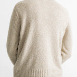 A person viewed from the back wearing a cream-colored knit sweater over a light gray shirt and teal pants, against a plain white background.