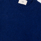 Close-up of a blue sweater with 'Folk' label on a light gray background