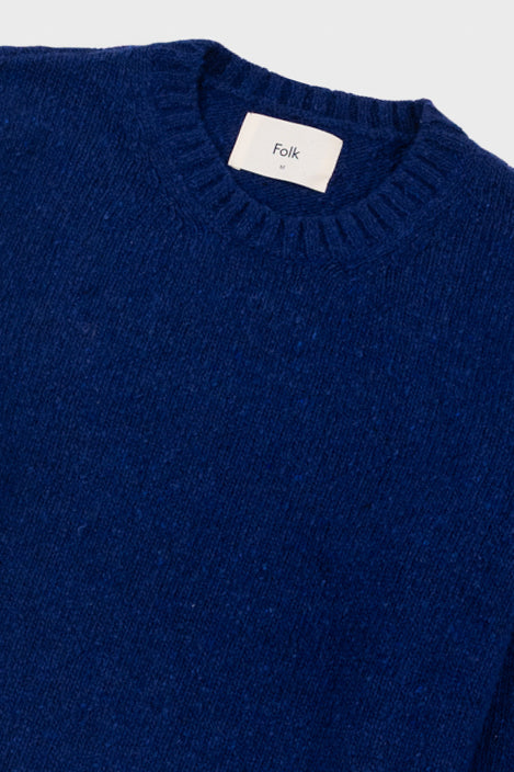 Close-up of a blue sweater with 'Folk' label on a light gray background