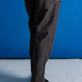 A person wearing dark charcoal gray slim-fit trousers, a white textured shirt, and black leather shoes, standing against a vibrant blue studio backdrop.