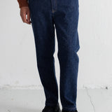 A person wearing dark blue straight-leg jeans, a rust-orange knit cardigan over a striped shirt, and black lace-up boots, standing against a white wall.