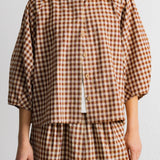 A person wearing a brown and beige gingham check dress with a white crew neck and white undershirt, shown from the neck down against a plain light background.