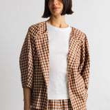 A model wearing a brown and beige gingham check blazer over a white t-shirt and matching gingham trousers, shot against a plain light gray background.