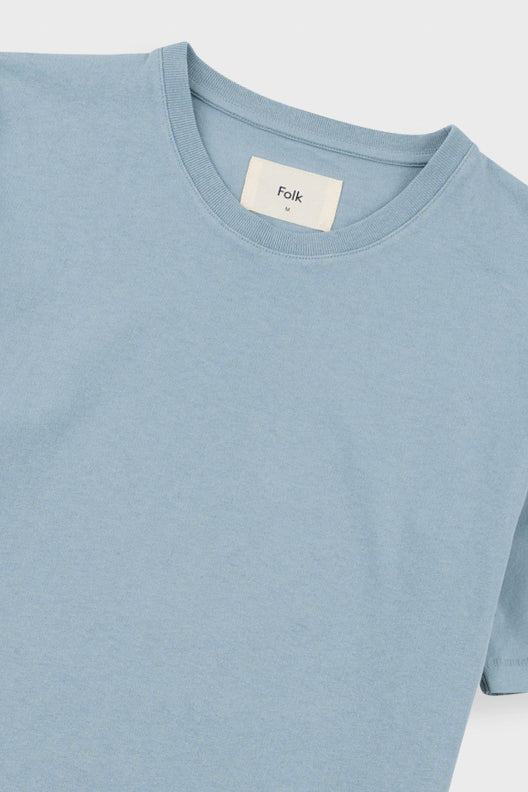 Close-up of a light blue crewneck t-shirt with a white neck label reading 'Folk'.