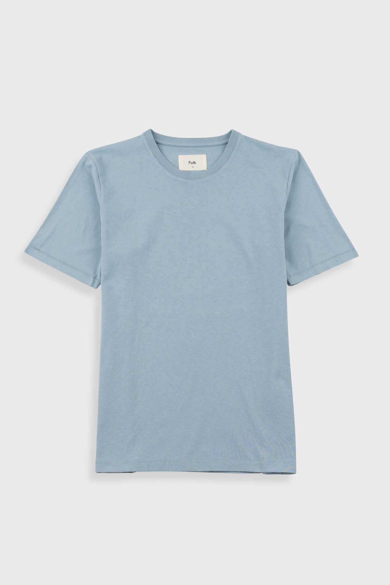 Close-up of a light blue crewneck t-shirt with a white neck label reading 'Folk'.