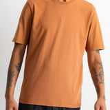 A man wearing a solid orange crew-neck t-shirt and black pants, shown from the waist up against a plain white background.