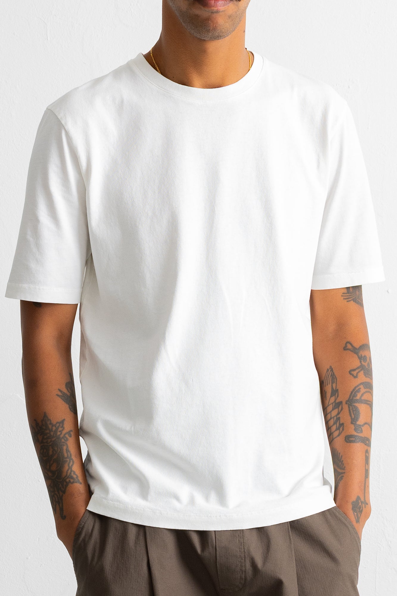A man wearing a plain white short-sleeve crewneck t-shirt, shown from the neck down against a light gray background.