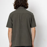 Person wearing a green shirt and black pants against a white background